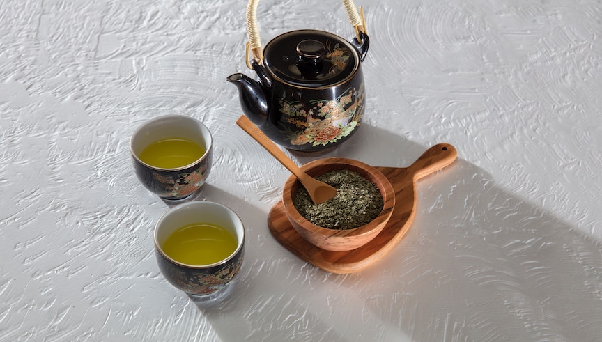 A green tea set comprising two tea cups, a teapot and a wooden bowl with tea leaves